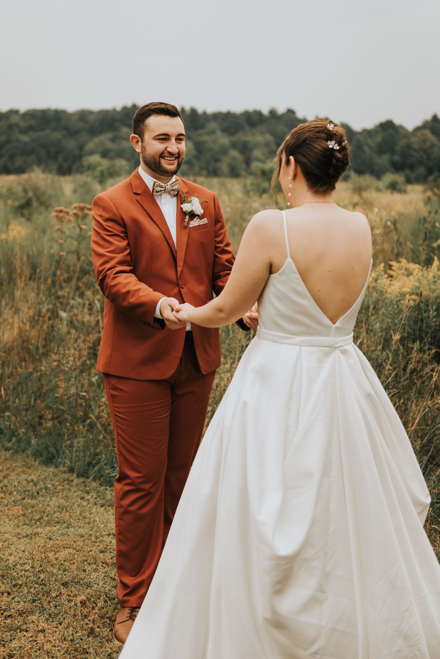 A couple shares a moment during their outdoor wedding ceremony, with the bride in white and groom in rust-colored suit.