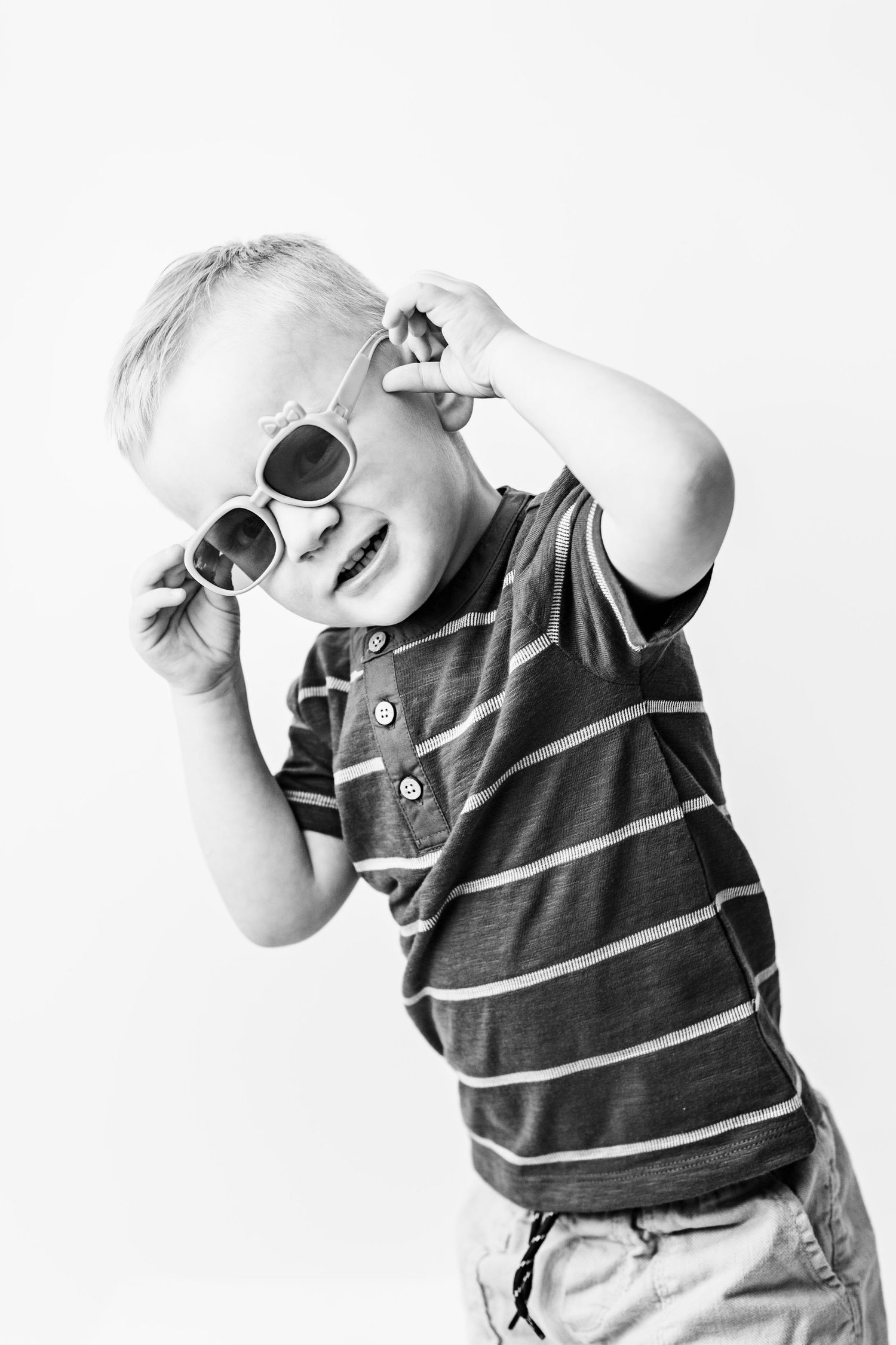 Black and white studio portrait of a young child with long hair and white ruffled clothing against light background.