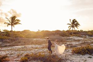 Bride and groom running through golden dunes at sunset in Tulum. Editorial wedding photography in Mexico.
