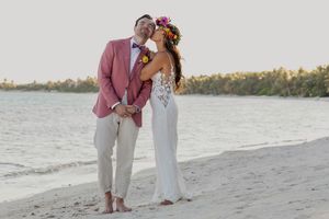 A romantic beach wedding ceremony with couple embracing on sandy shore at sunset by the ocean.