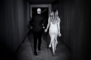 A couple walking down a dark hallway, with the woman wearing a light dress and the man in a dark suit.