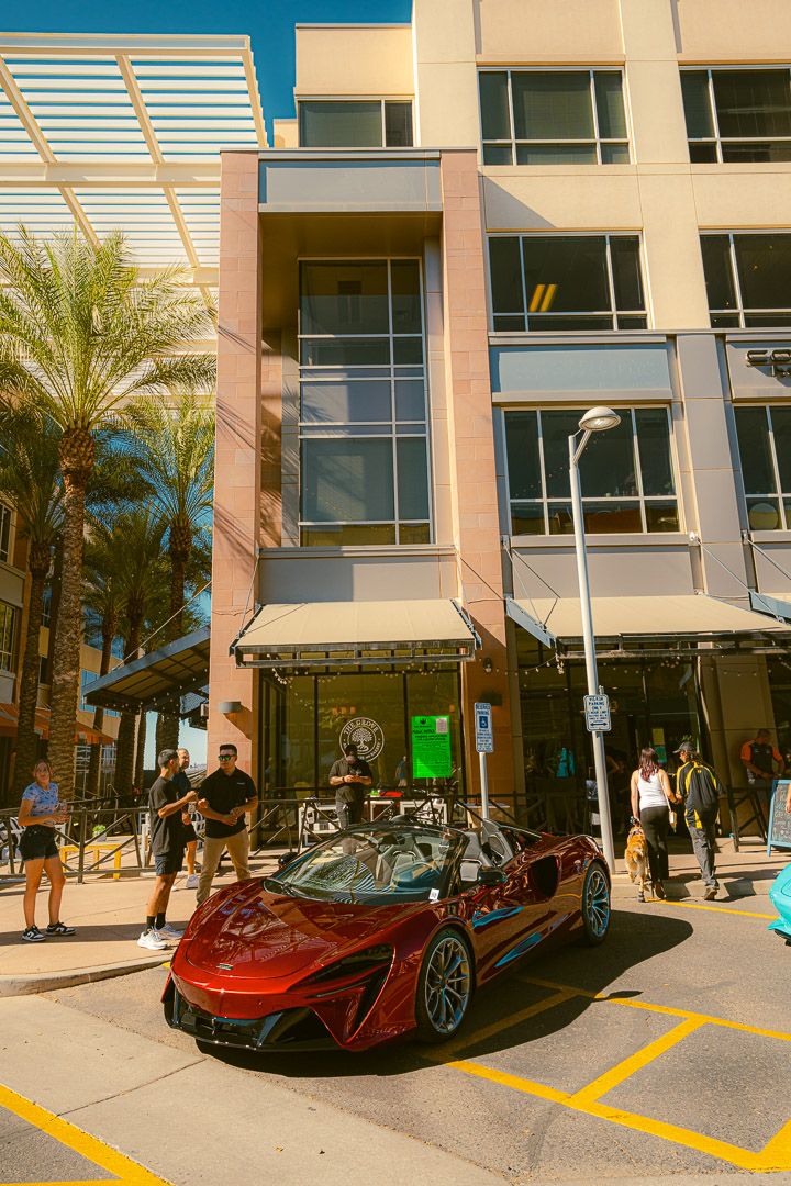 Luxury sports cars including a McLaren and other exotic vehicles parked in front of a modern building with palm trees.