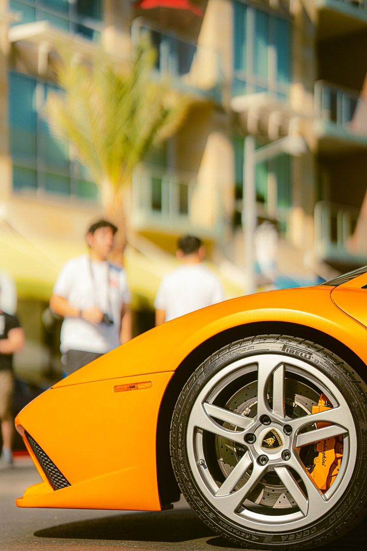 Close-up view of a bright orange Lamborghini sports car's alloy wheel and brake caliper on a sunny street.