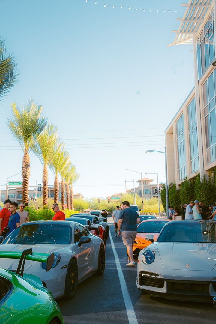 High-end exotic supercars parked in a row outside a contemporary building with palm trees and blue skies overhead.