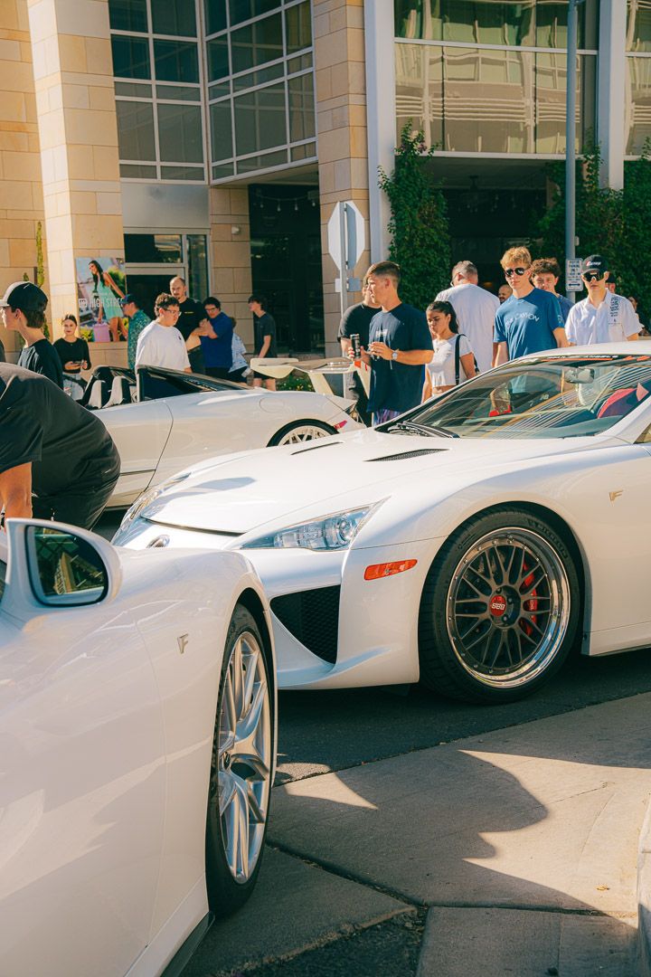 Collection of high-end white sports cars on display at a car meet with spectators gathering around.