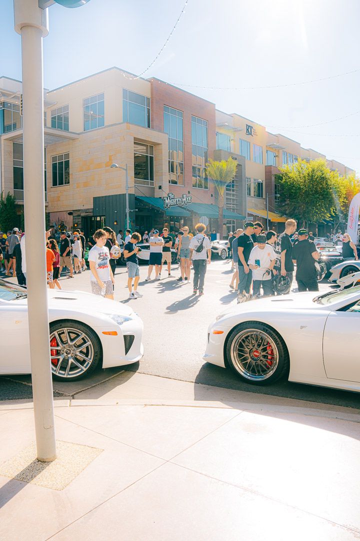 White sports cars line up at an outdoor car show event with crowds of spectators gathering to view the vehicles.