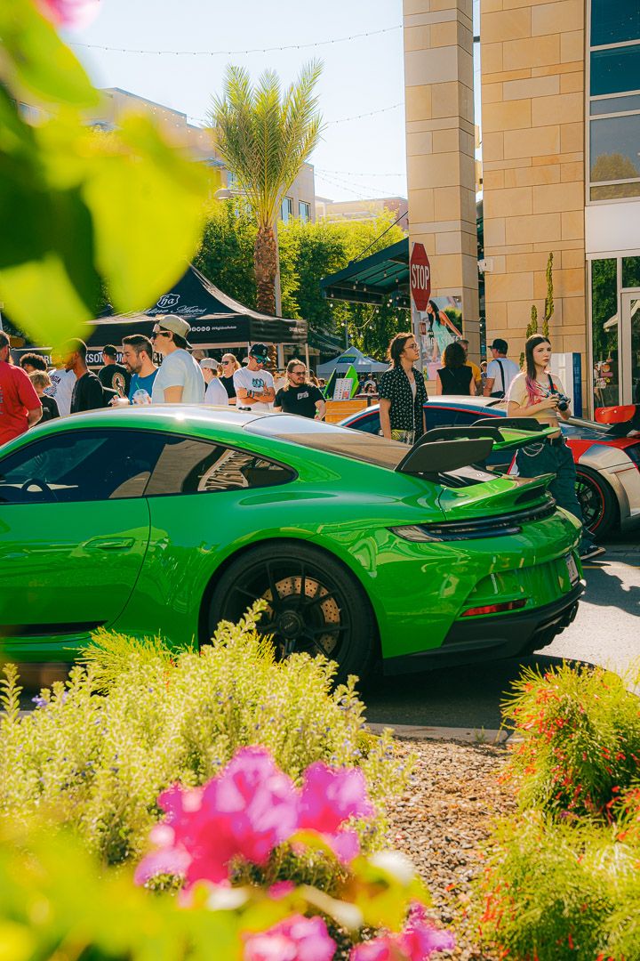 A vibrant green supercar showcased among colorful flowers and landscaping at a daytime car exhibition.