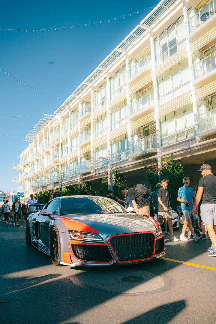 Luxury sports cars lined up for display at a car meet under blue skies and string lights.