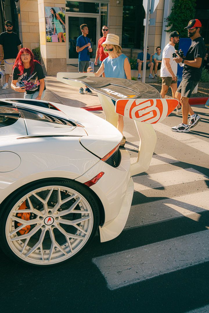 A white sports car with intricate aftermarket wheels on display at an outdoor car show.