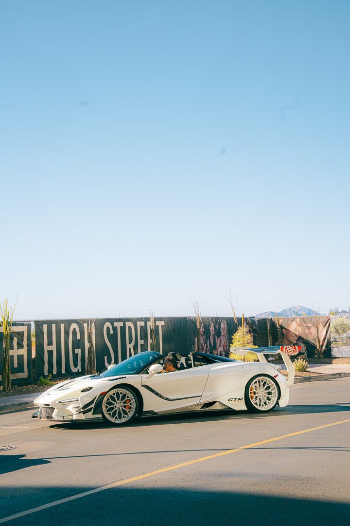 Sleek silver McLaren convertible parked on High Street with desert mountains in the background.