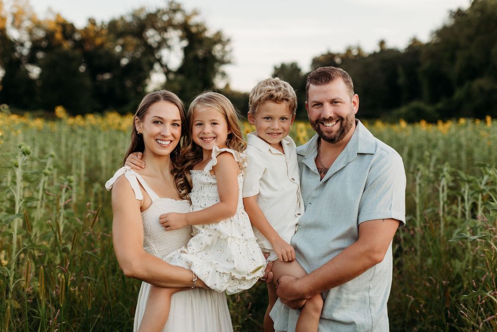 Family portrait session in a sunlit field with sunflowers during golden hour.