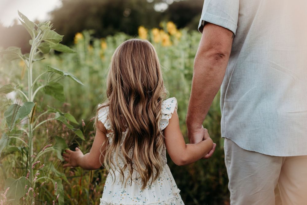 Side view of two people walking hand in hand through a sunflower field at sunset.
