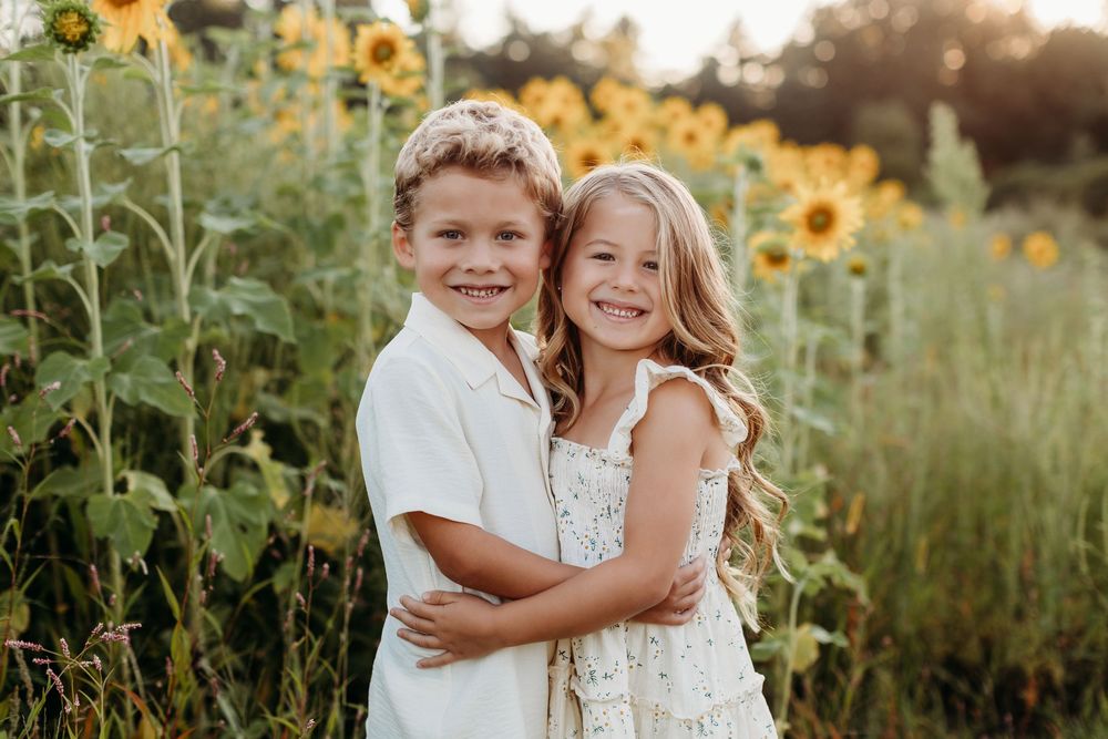 Children playing and laughing together in a sunflower field at golden hour.