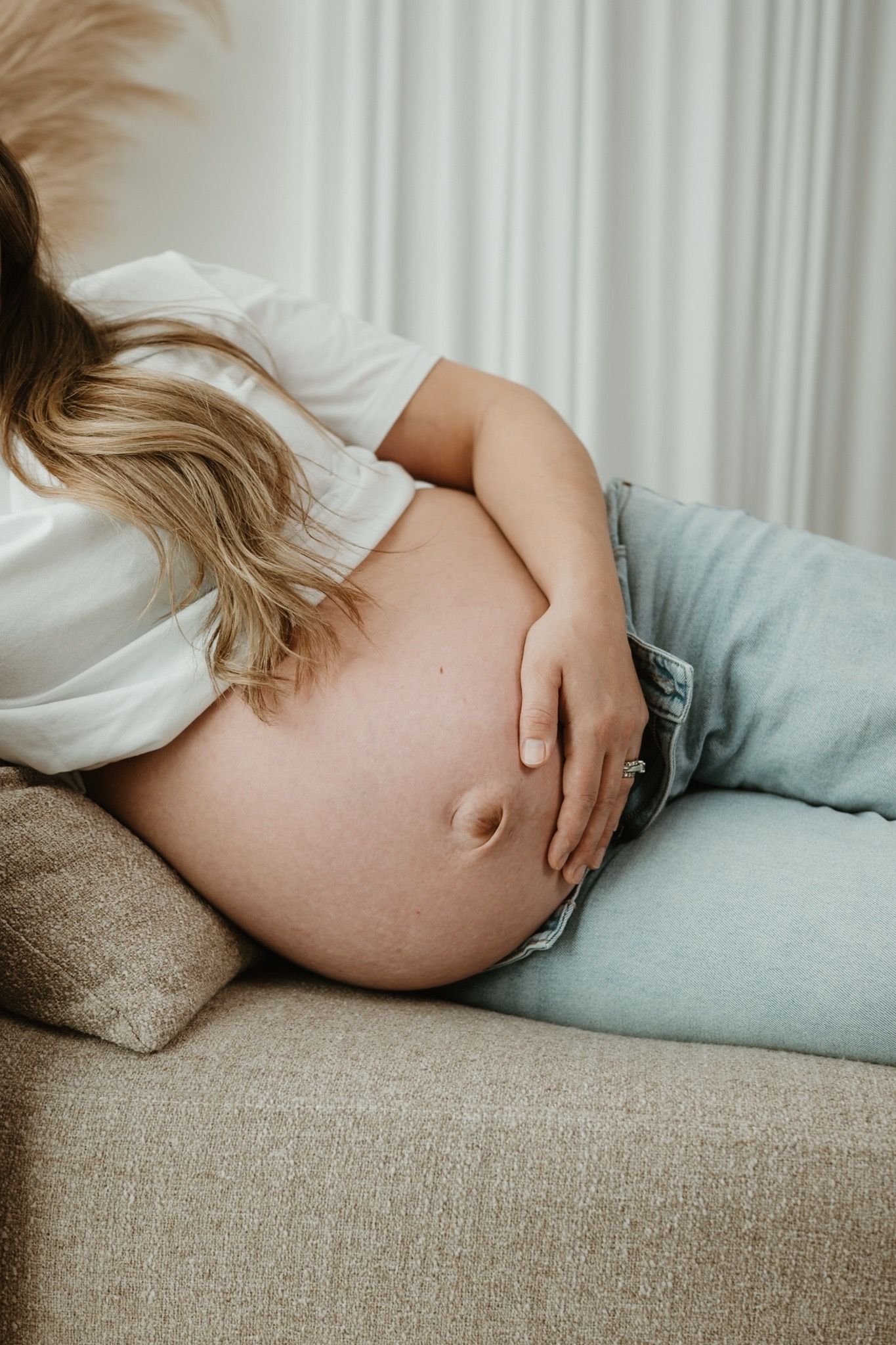 Four cropped torso photos showing a woman in maternity clothes and jeans resting her hand against her pregnant stomach. Regina maternity.