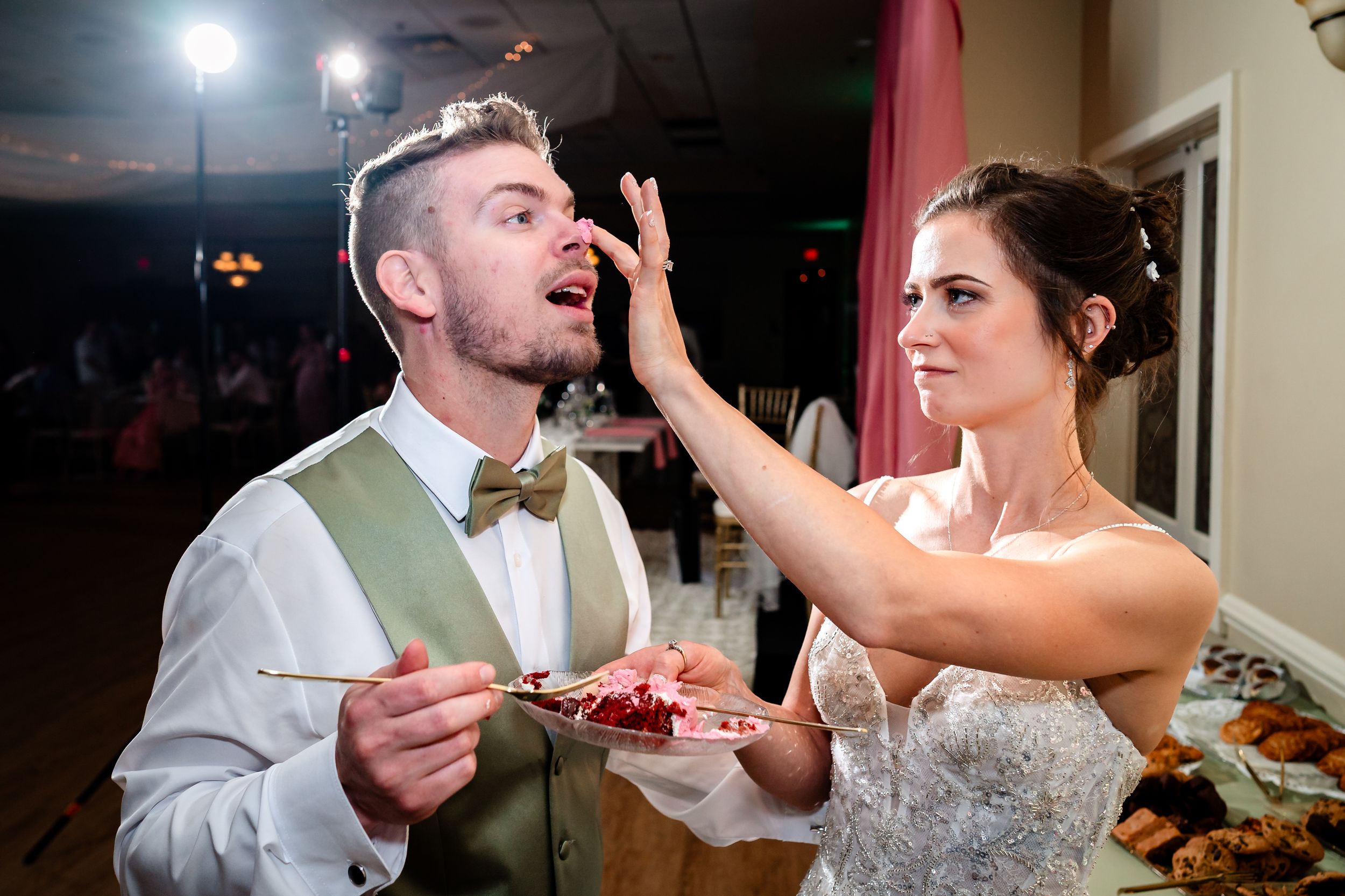 Wedding couple laughs while messily feeding each other cake at their reception.