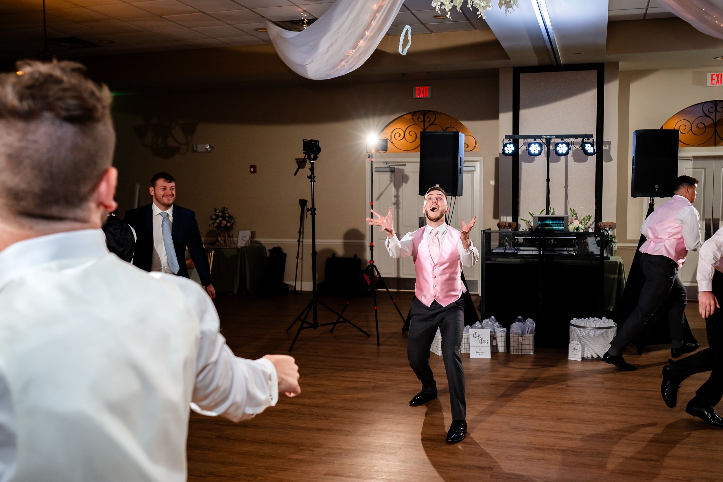 Wedding guests dance and celebrate in a spacious reception venue with wooden floors.