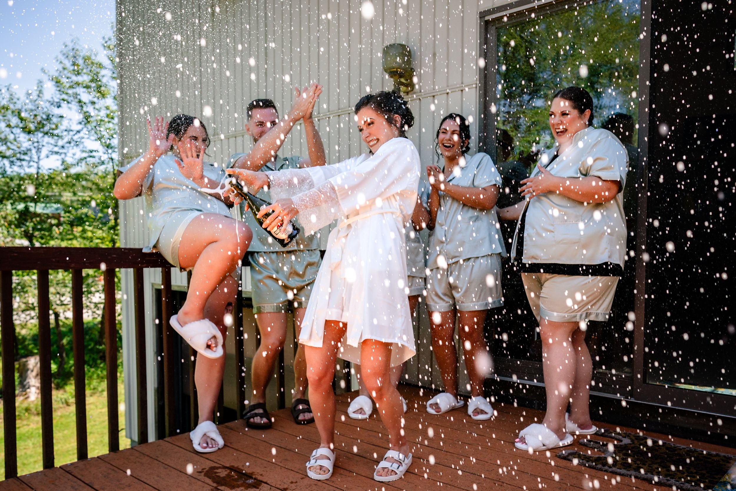 Wedding party celebrating outdoors with champagne spraying in slow motion.