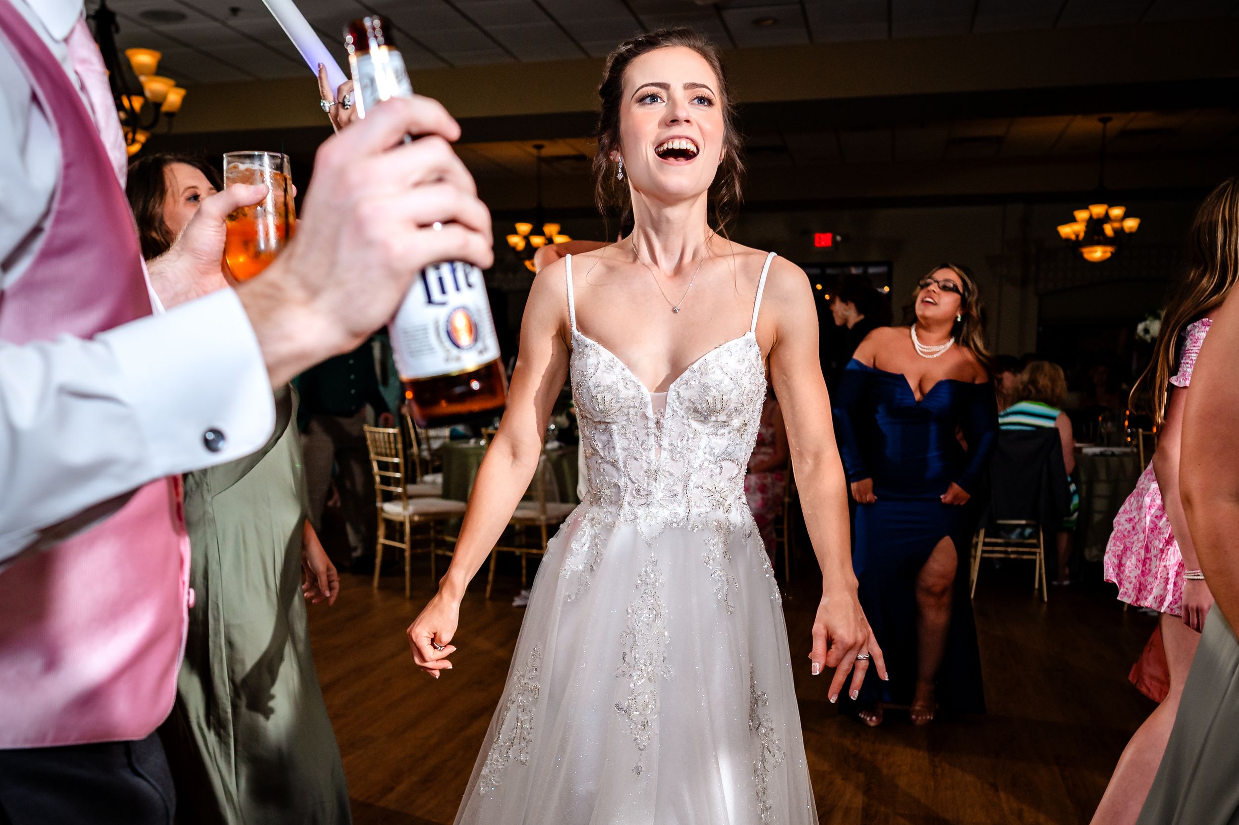 Bride in white lace dress laughing and dancing during wedding reception.