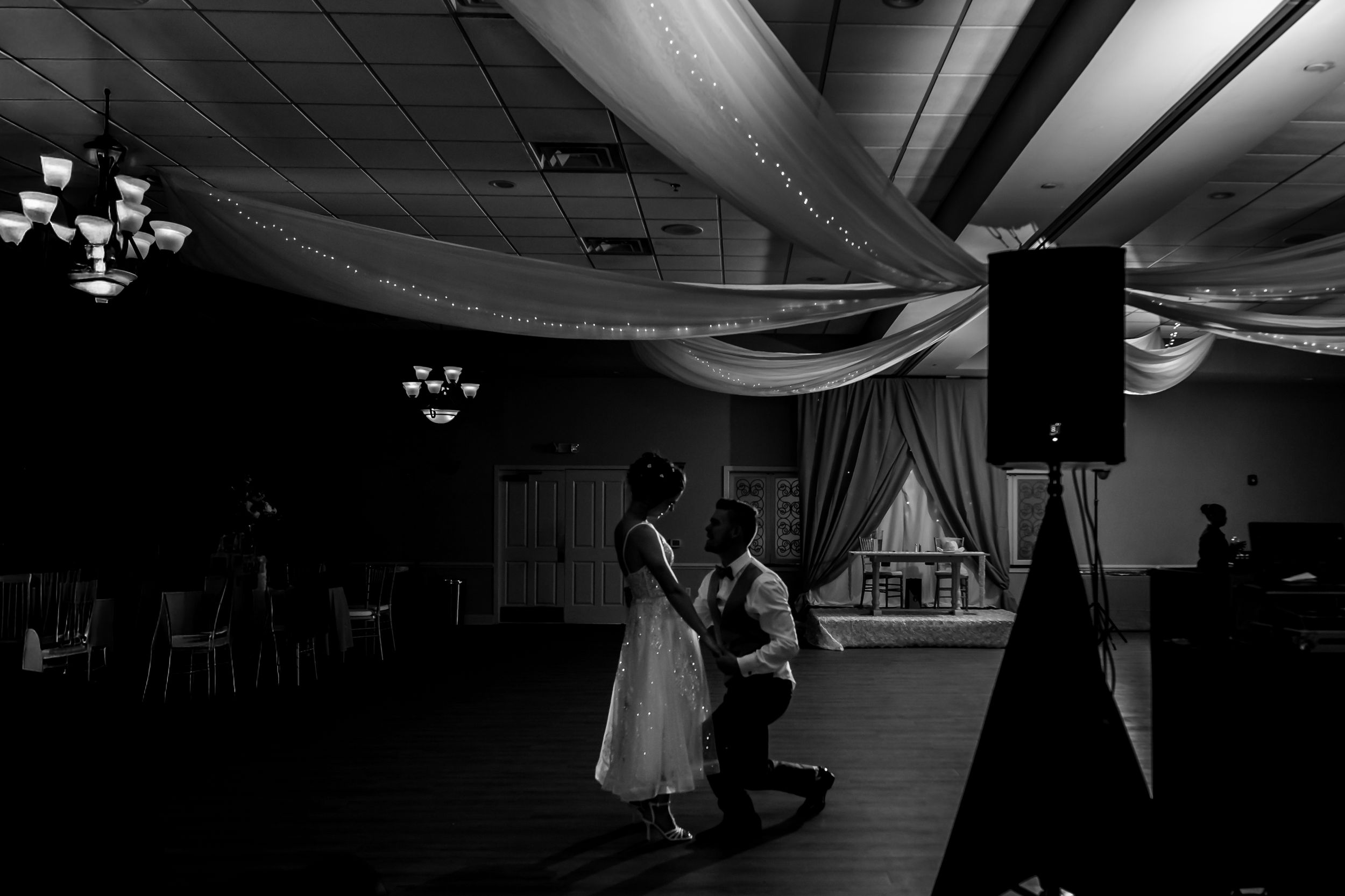 Black and white artistic shot of wedding reception venue with dramatic lighting.