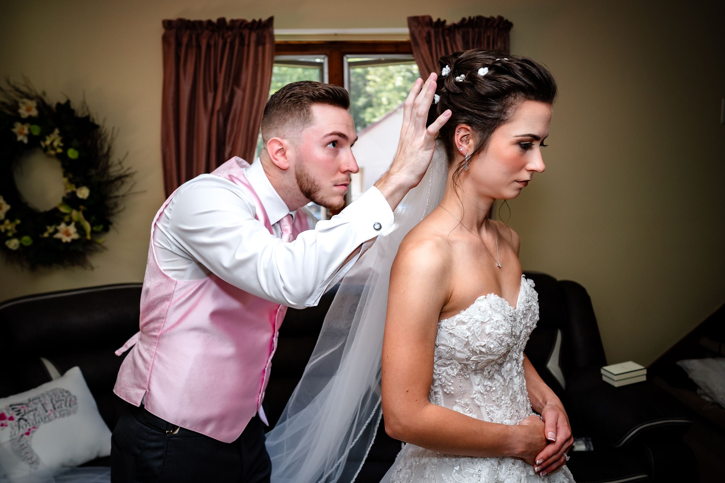 An emotional wedding moment captured indoors with soft lighting and curtains in the background.