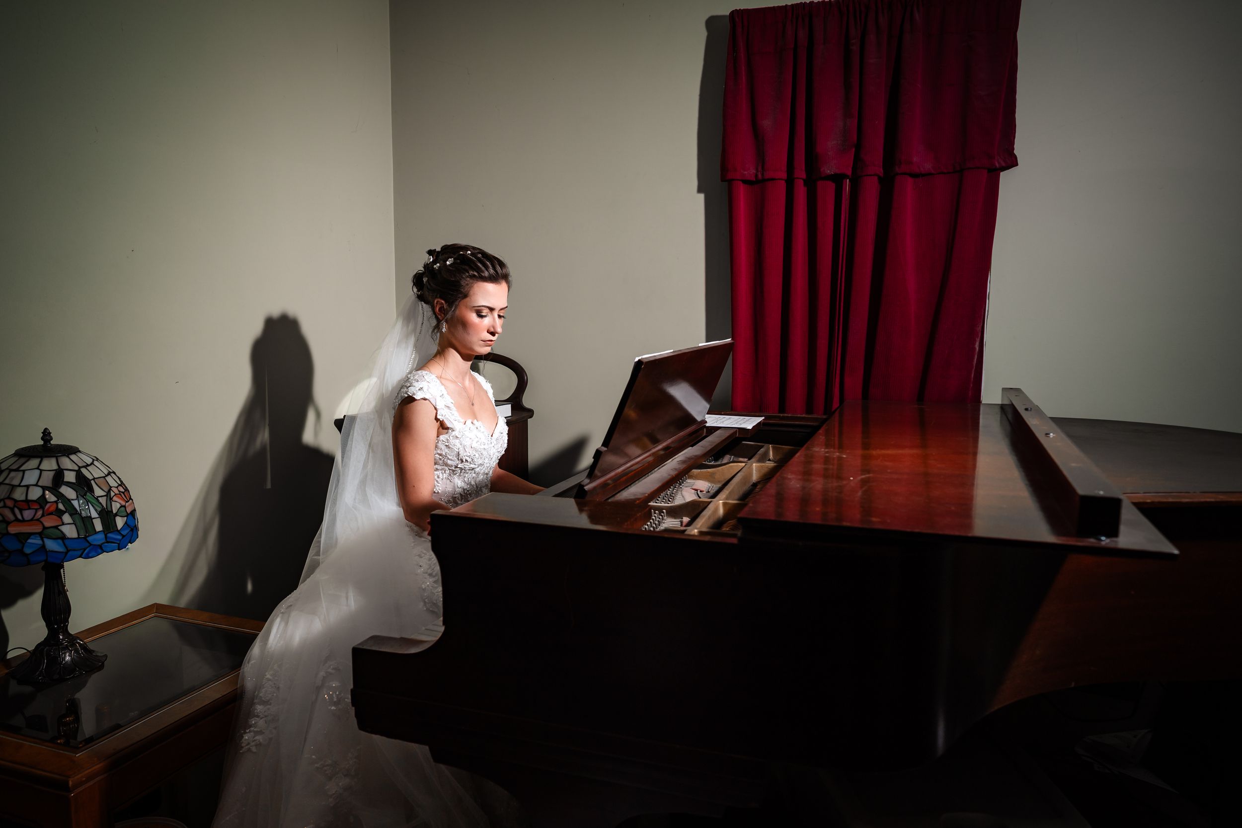 Wedding preparation scene in a room with dark red curtains and dramatic lighting.