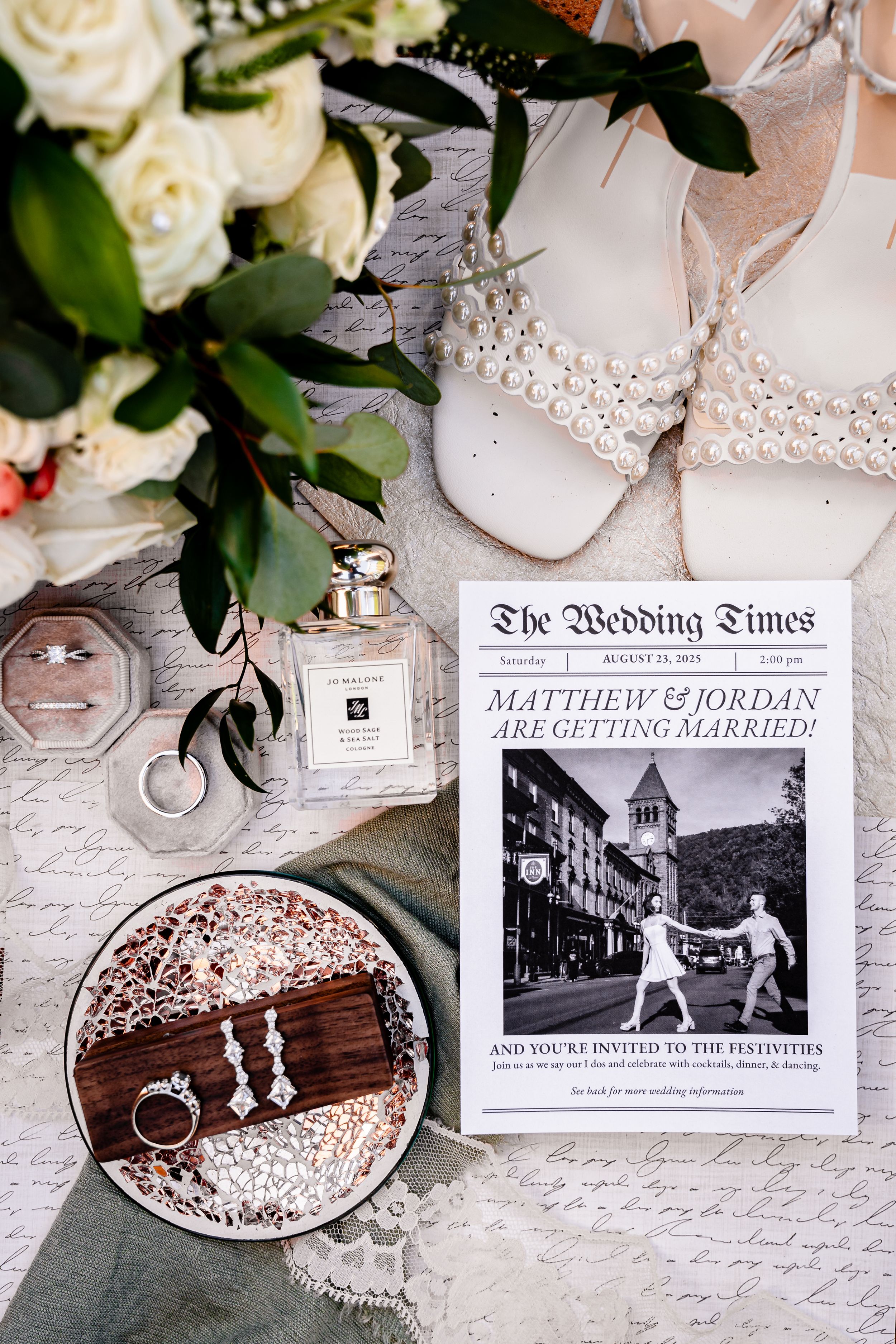 Wedding details including rings, shoes, invitations and floral arrangements laid out in an elegant flat lay composition.