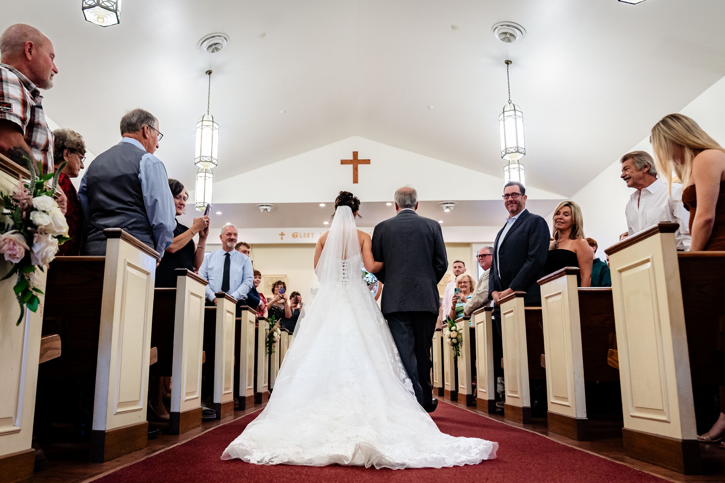 Church wedding ceremony with guests seated in wooden pews and white decor.