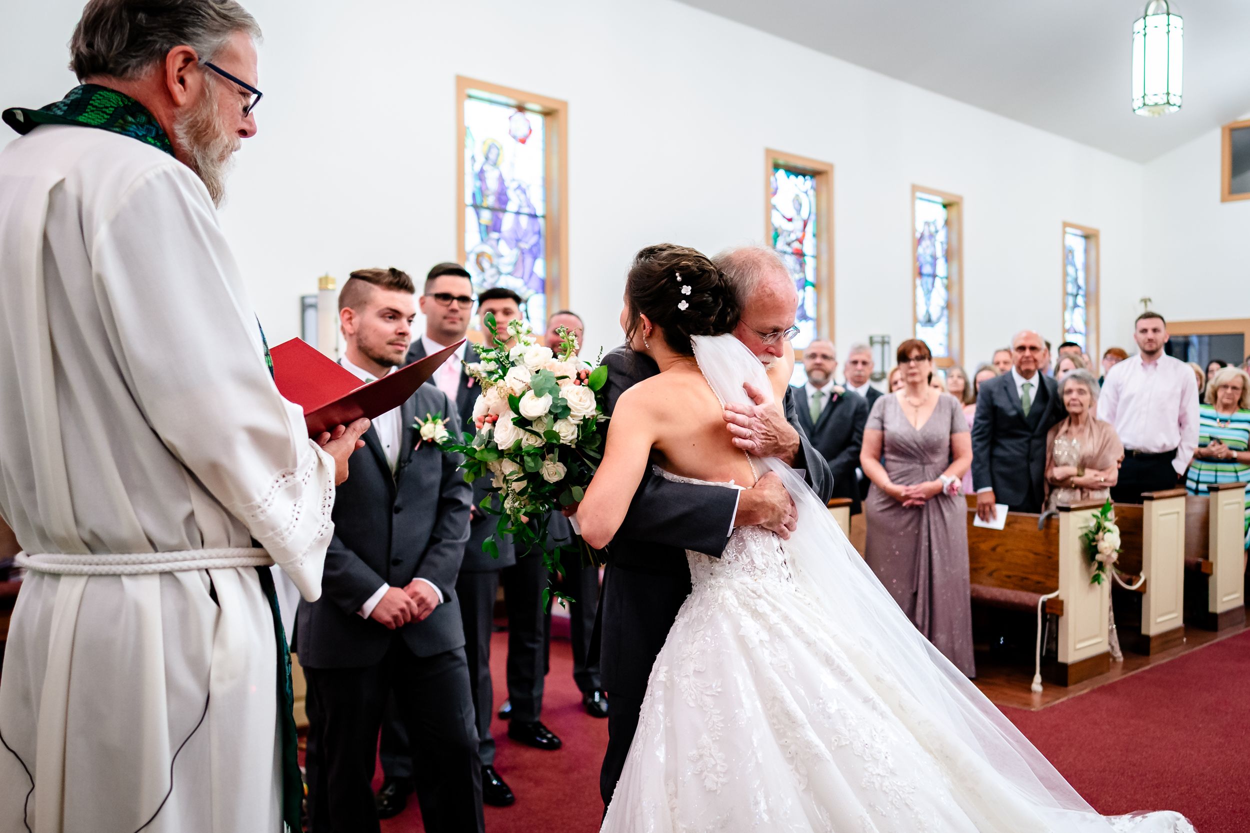 Wedding ceremony in progress at a church with red carpet and white decor.