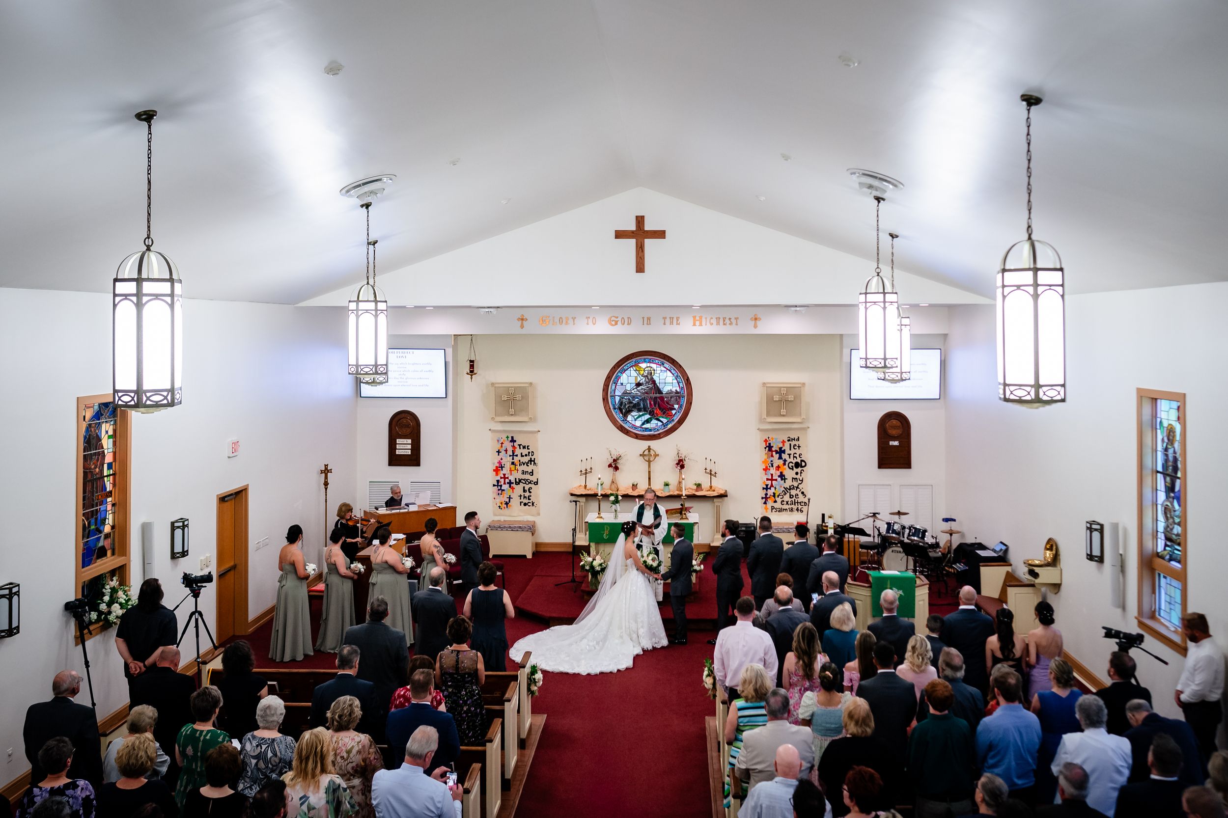 Wide angle view of a church wedding ceremony with guests seated in wooden pews.