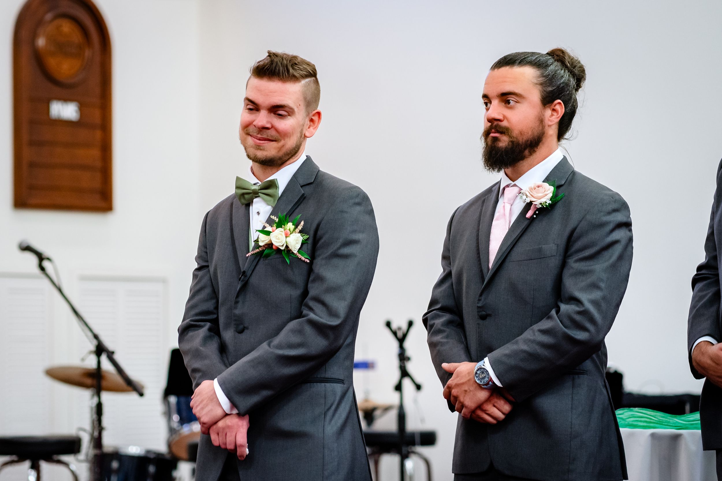 Groomsmen in charcoal gray suits stand together during wedding ceremony at church.