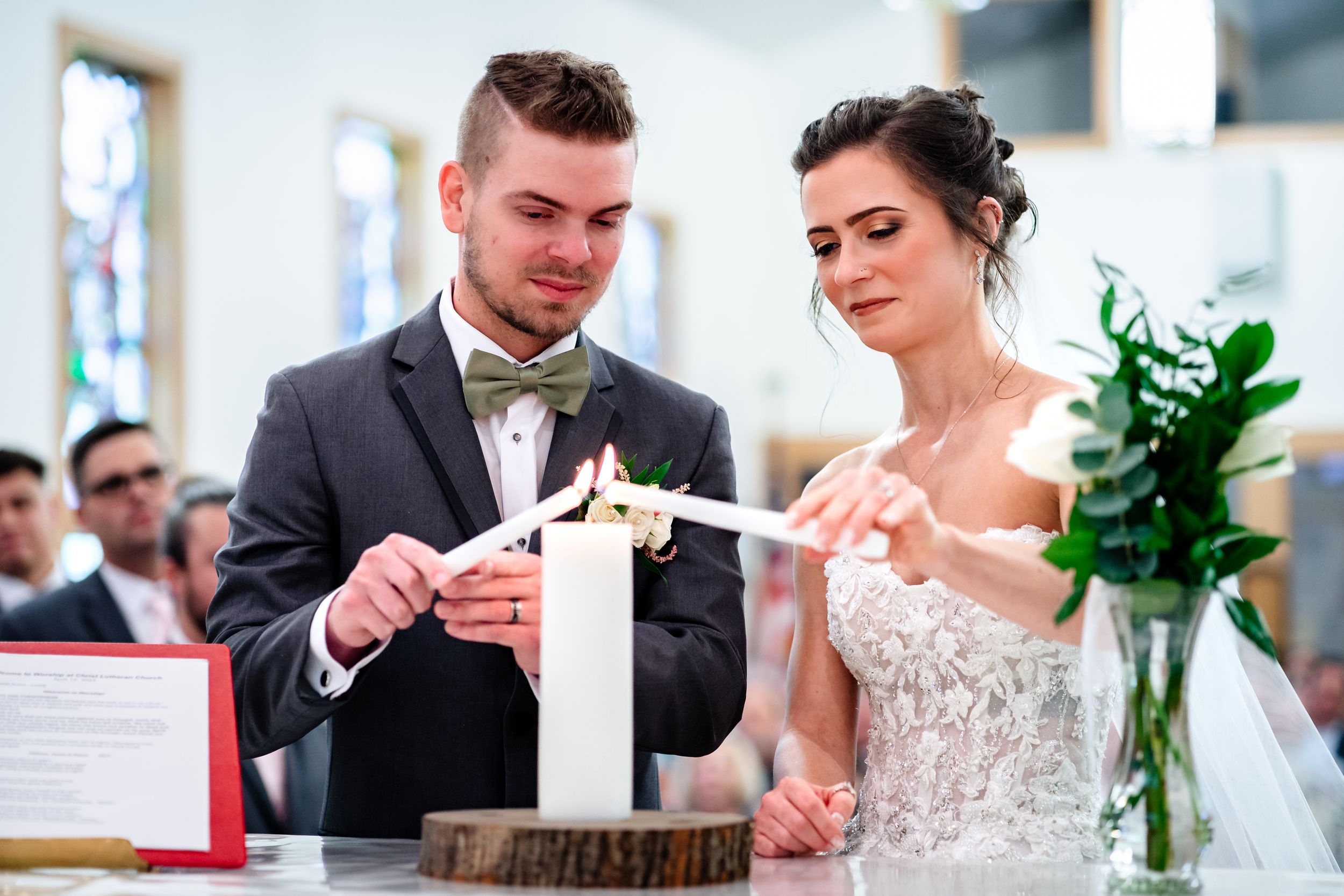 Wedding ceremony in church with couple exchanging vows at altar with stained glass windows.