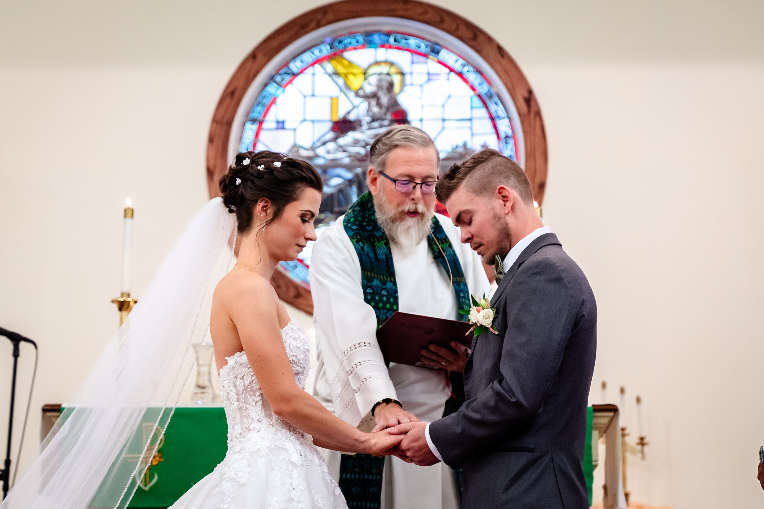 Traditional church wedding ceremony with decorative stained glass windows and green altar cloth.