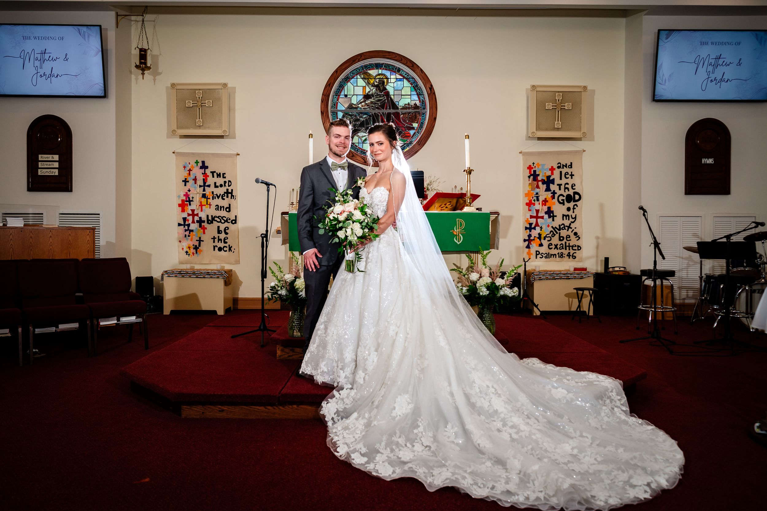 Church sanctuary decorated for wedding ceremony with stained glass windows and red carpet.