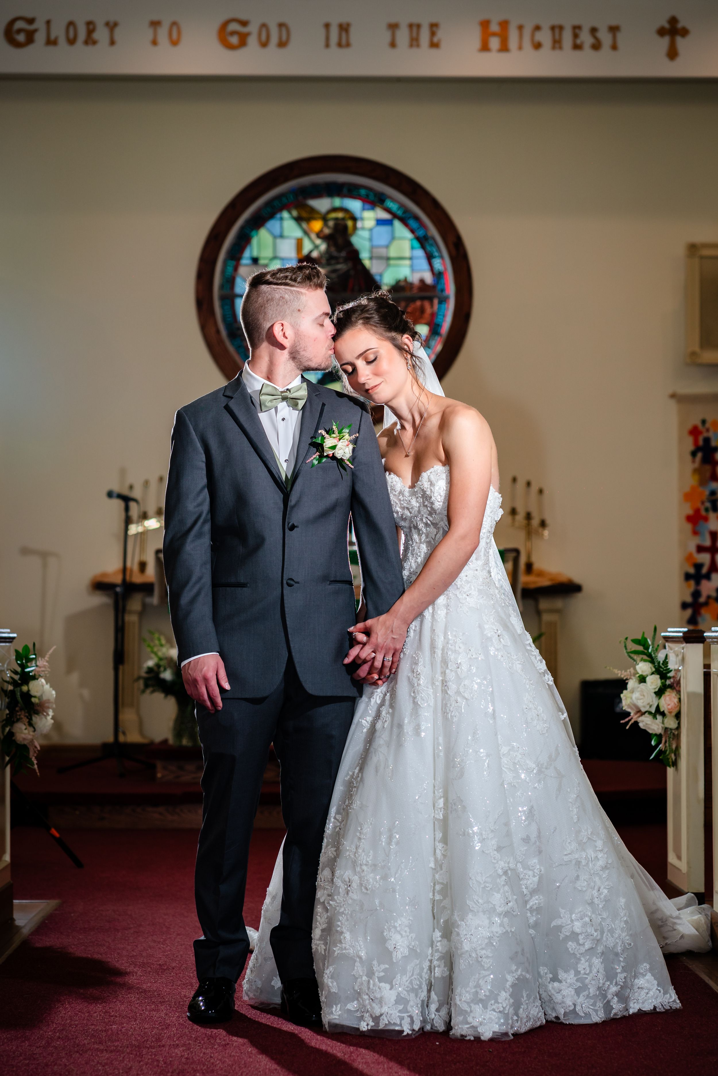 Church wedding ceremony under Glory to God sign with stained glass windows.