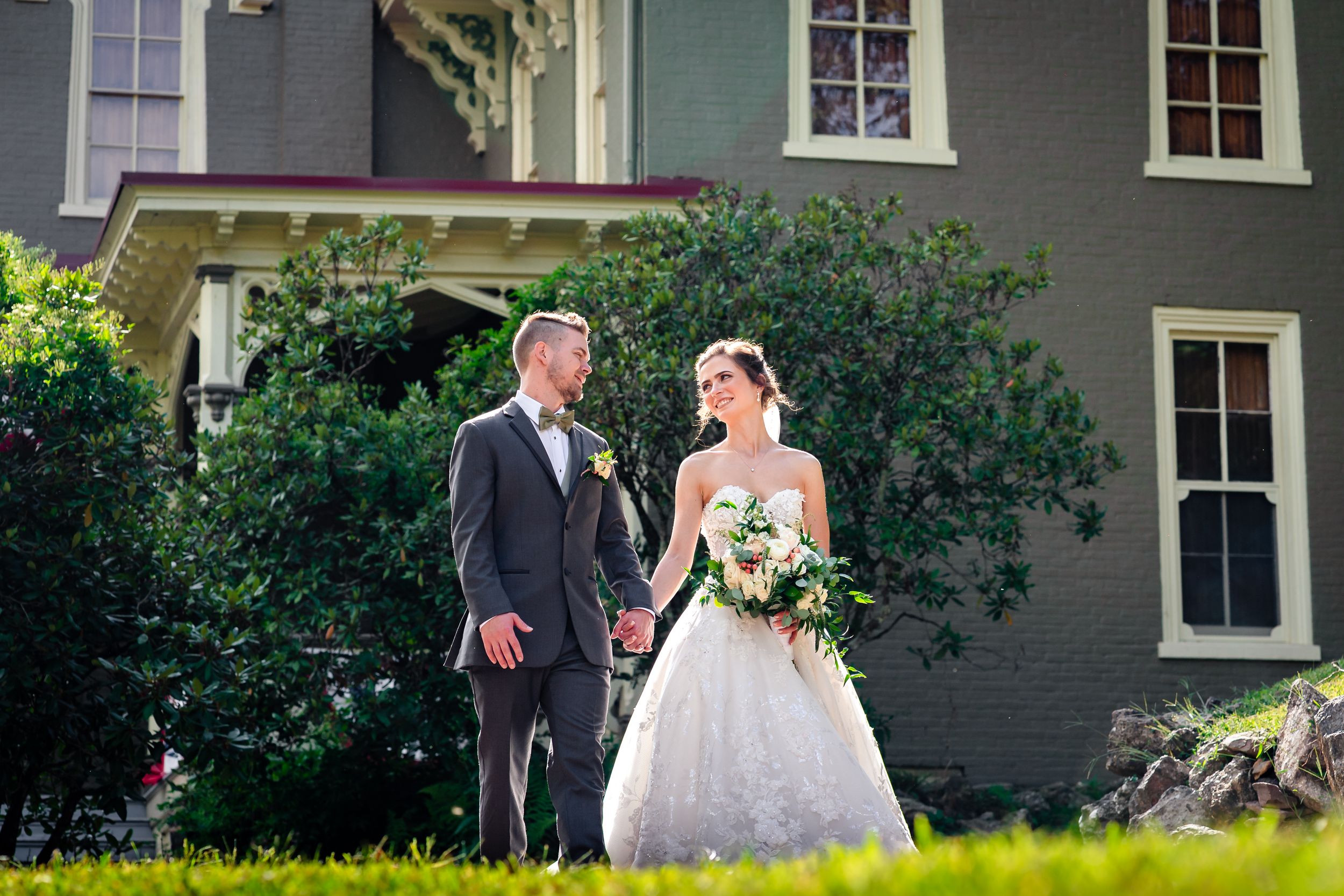 Wedding party poses in front of grey house with white trim and green landscaping.