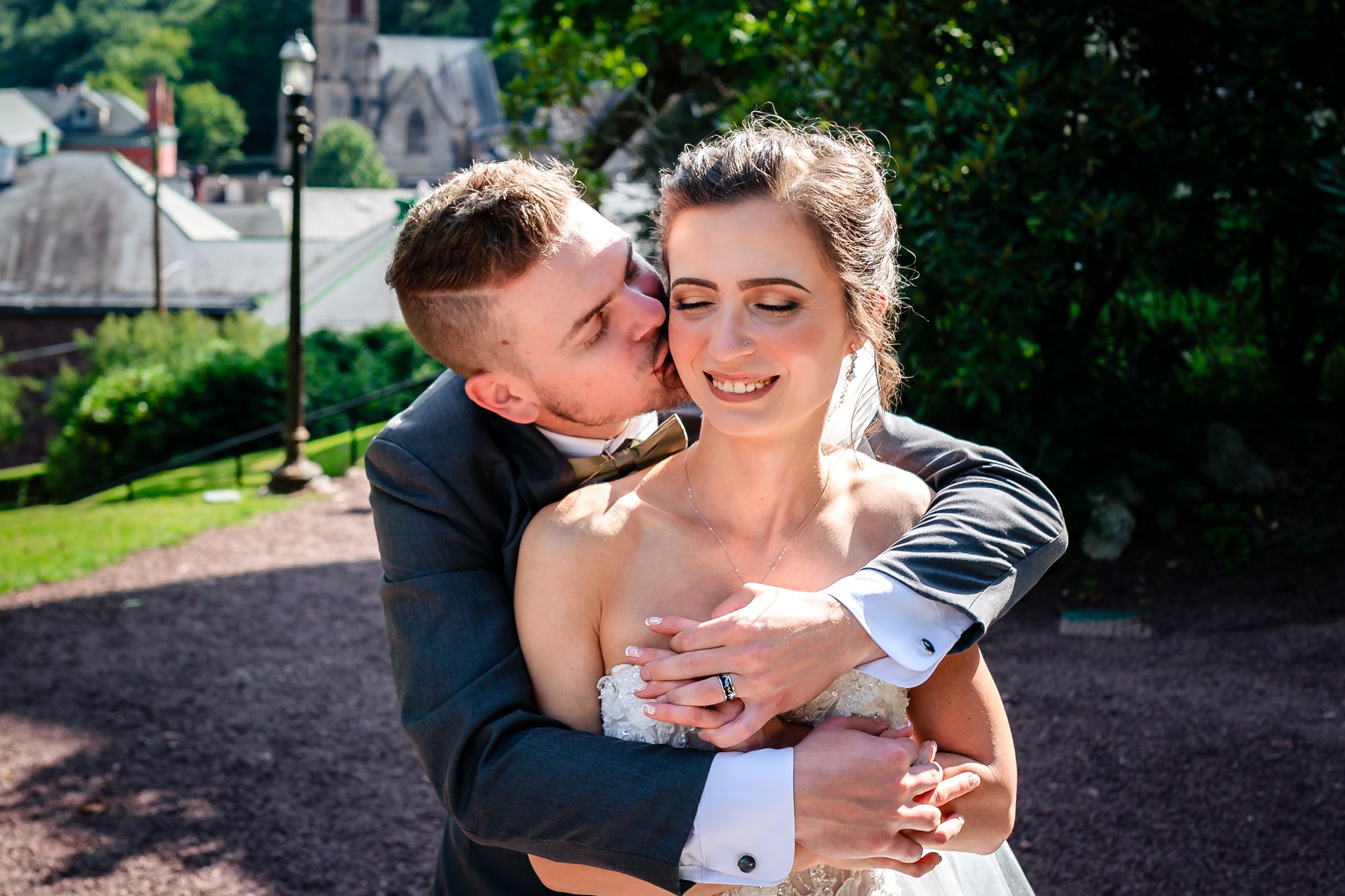Romantic wedding couple embraces in outdoor garden setting.