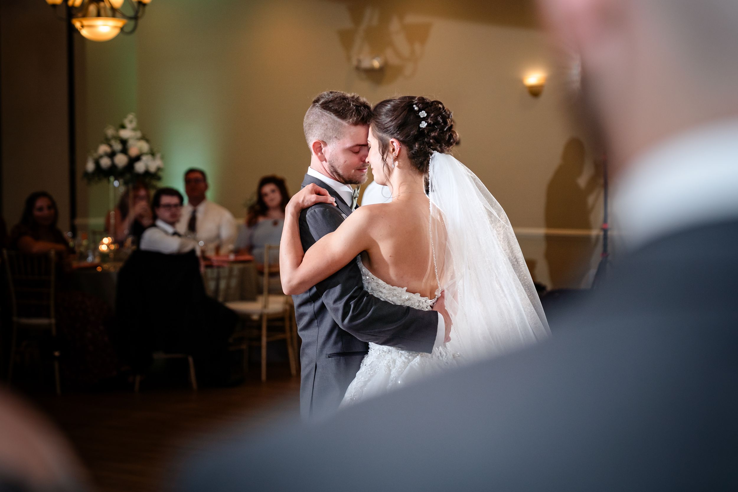 A tender first dance moment captured at a wedding reception with soft lighting and guests in the background.