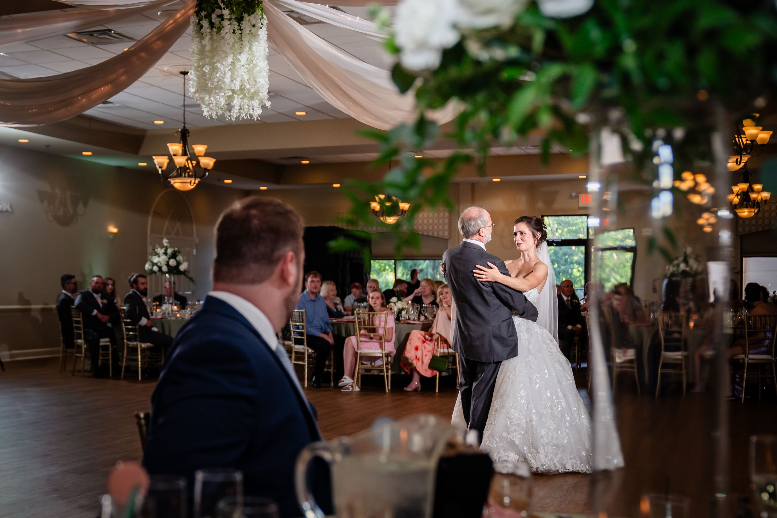 Wedding reception dance floor scene with elegant white draping and floral decorations overhead.