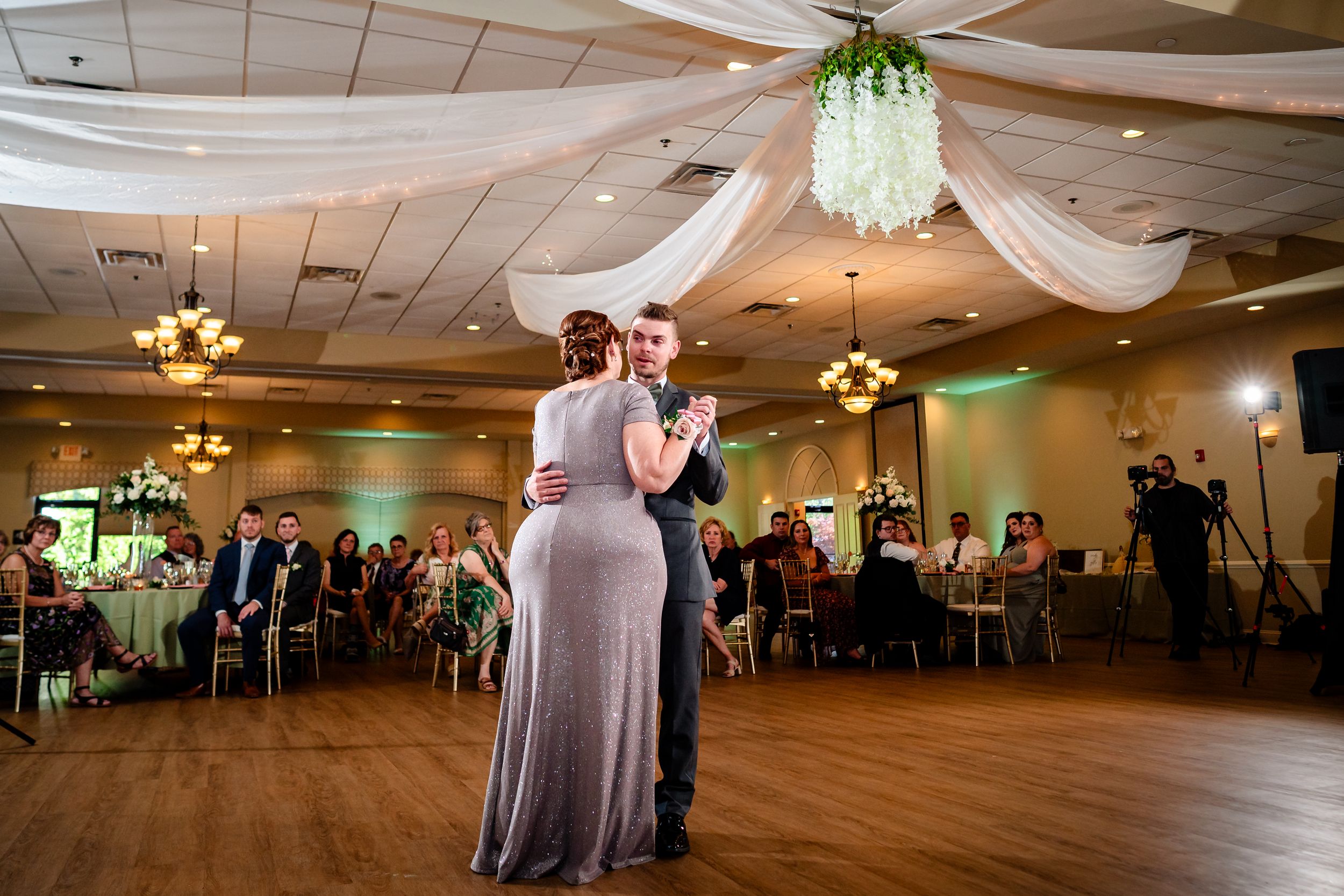 Wedding reception dance under draped fabric ceiling with warm lighting and round guest tables.
