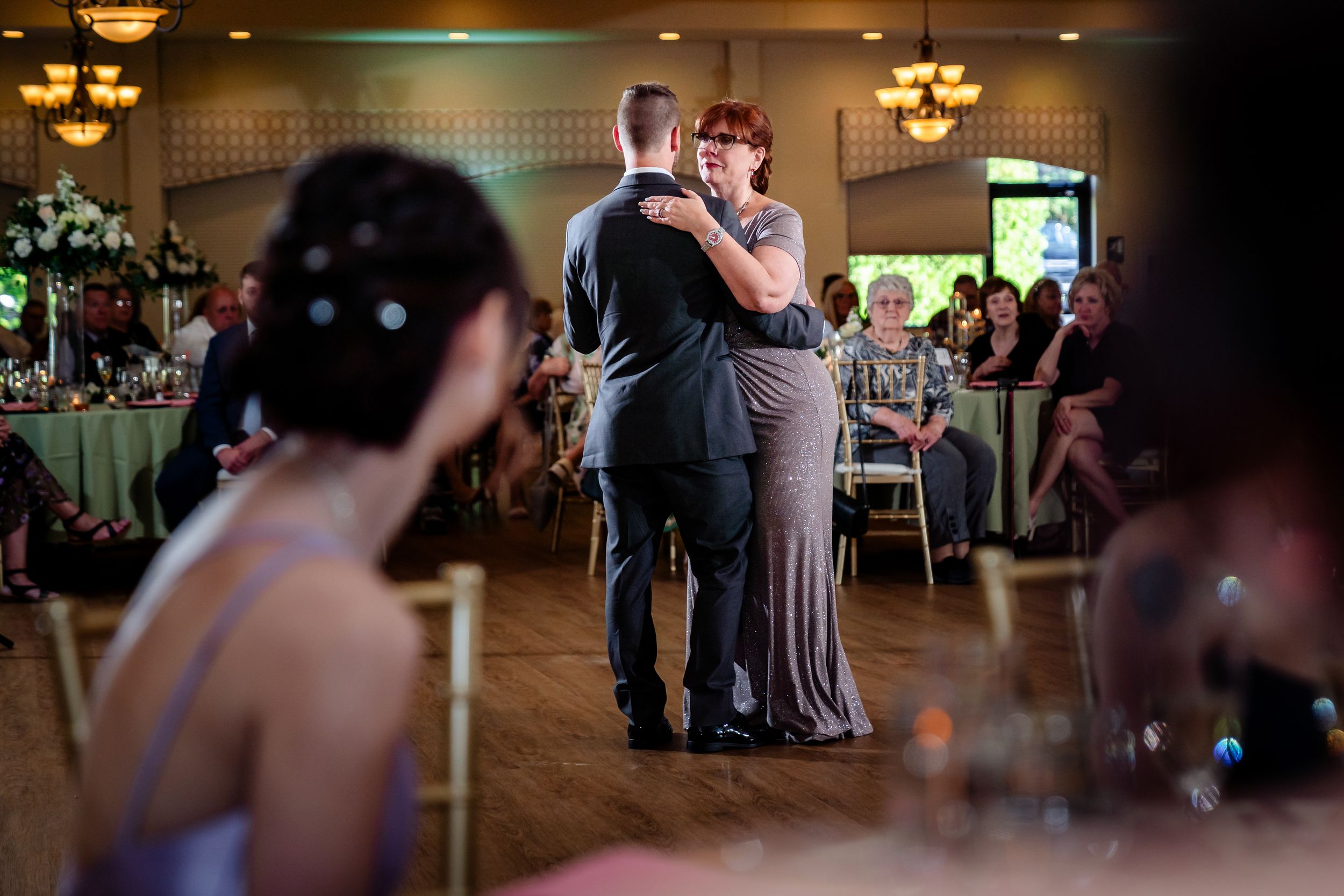 Wedding reception dance captured from across the room with table settings in foreground.