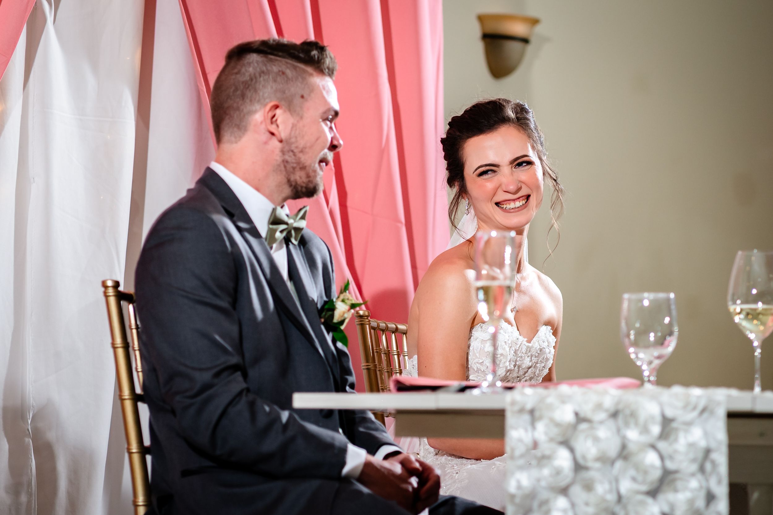 Candid reception moment at decorated sweetheart table with pink backdrop and table settings.