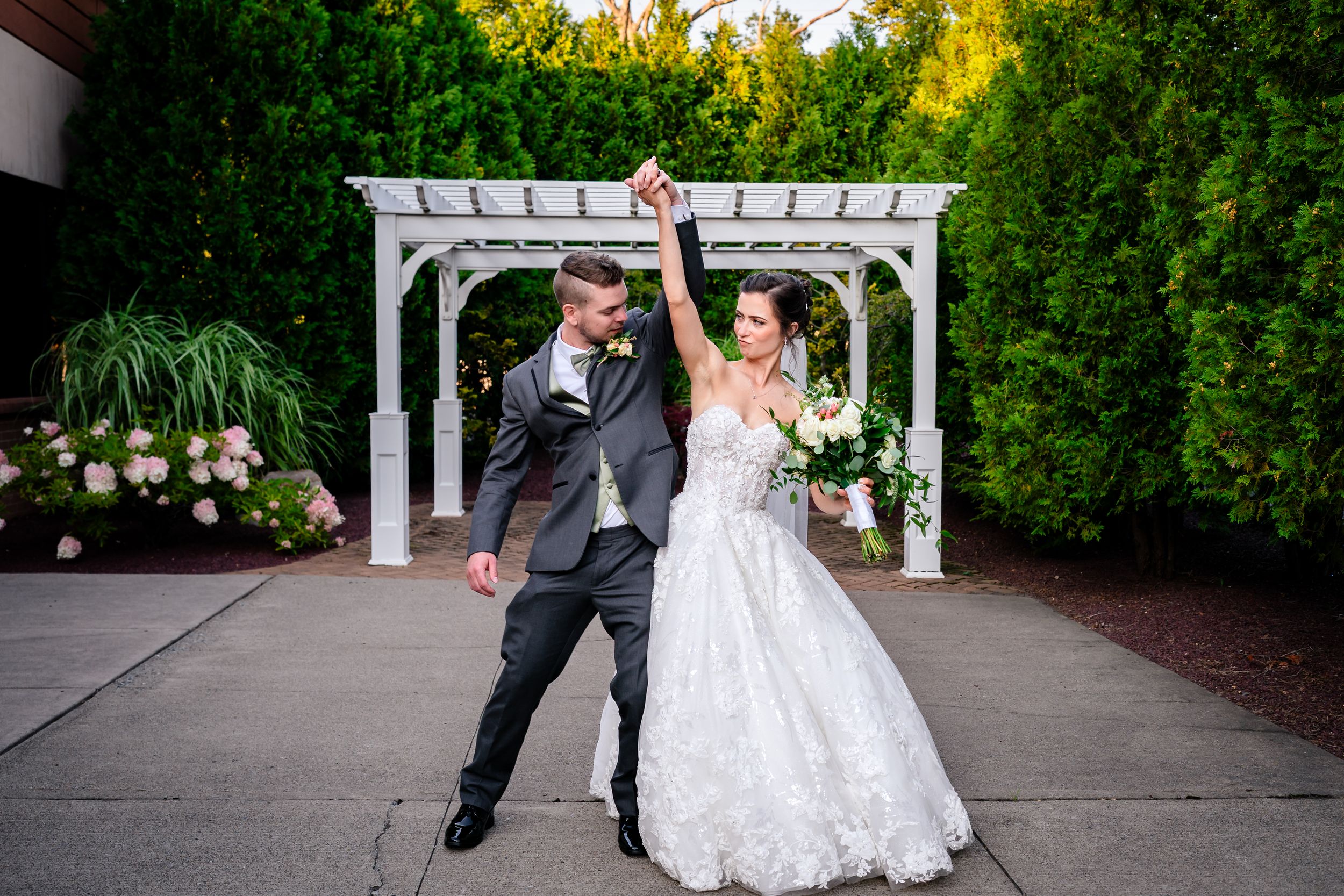 Newlyweds celebrate under a white garden pergola surrounded by greenery.