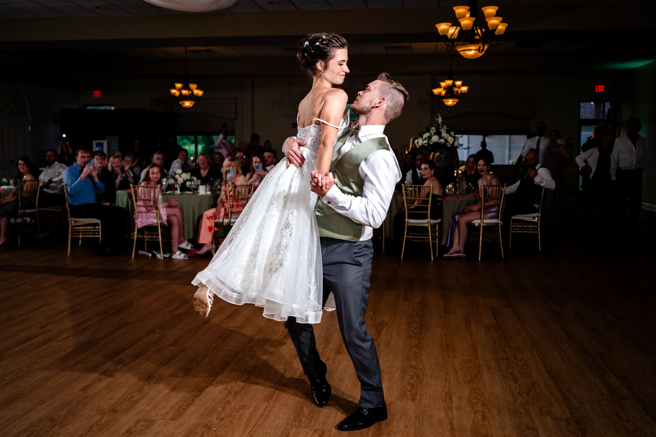 Couple performs a dramatic dance lift during their wedding reception on wooden dance floor.