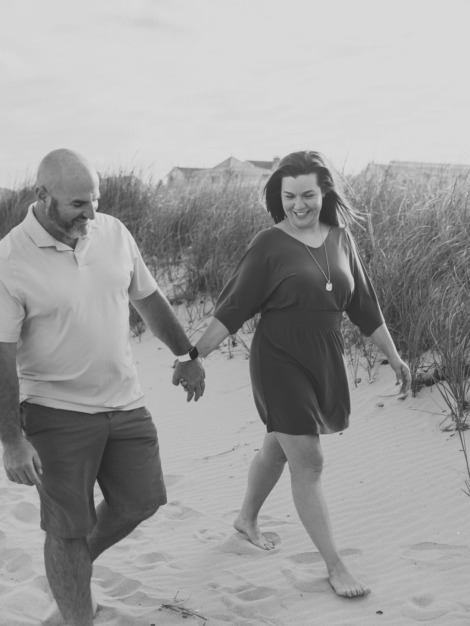 Black and white image of parents walking on the beach in Spring Lake NJ holding hands.