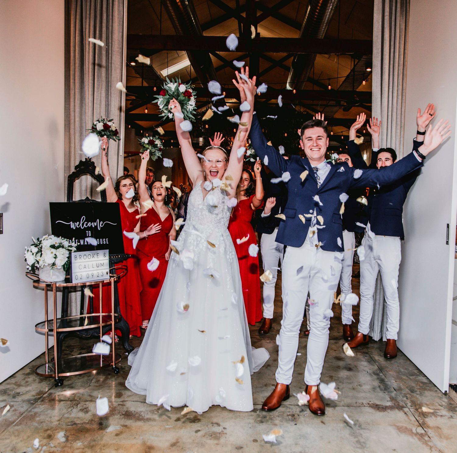 Wedding party celebrates with joy while tossing confetti in a hallway during an energetic exit celebration.