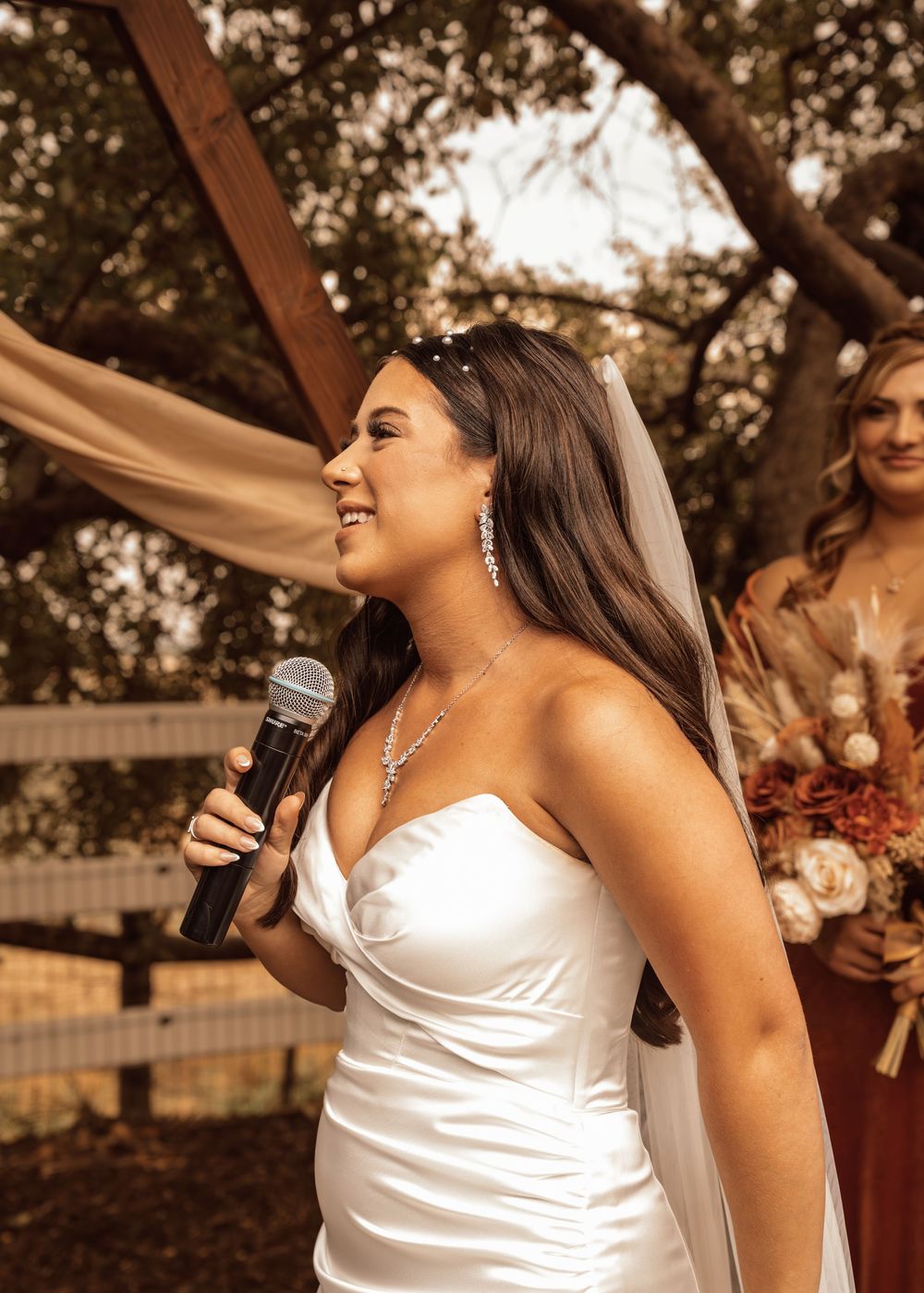 A bride speaking into microphone during an outdoor wedding ceremony.