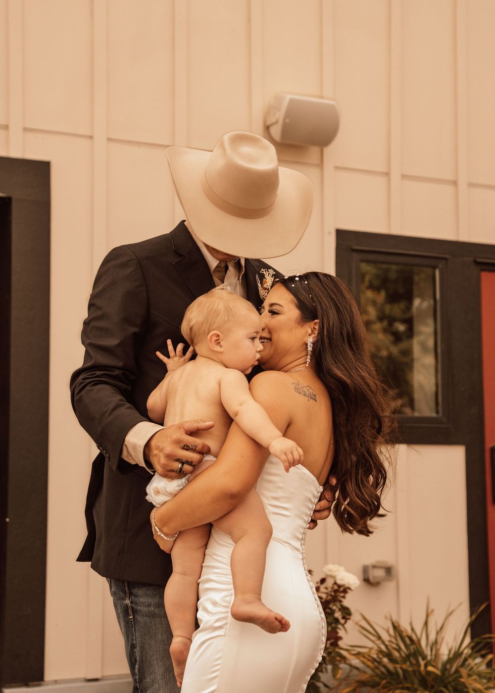 A tender moment between a couple and baby at a wedding celebration, with the bride in a white dress.