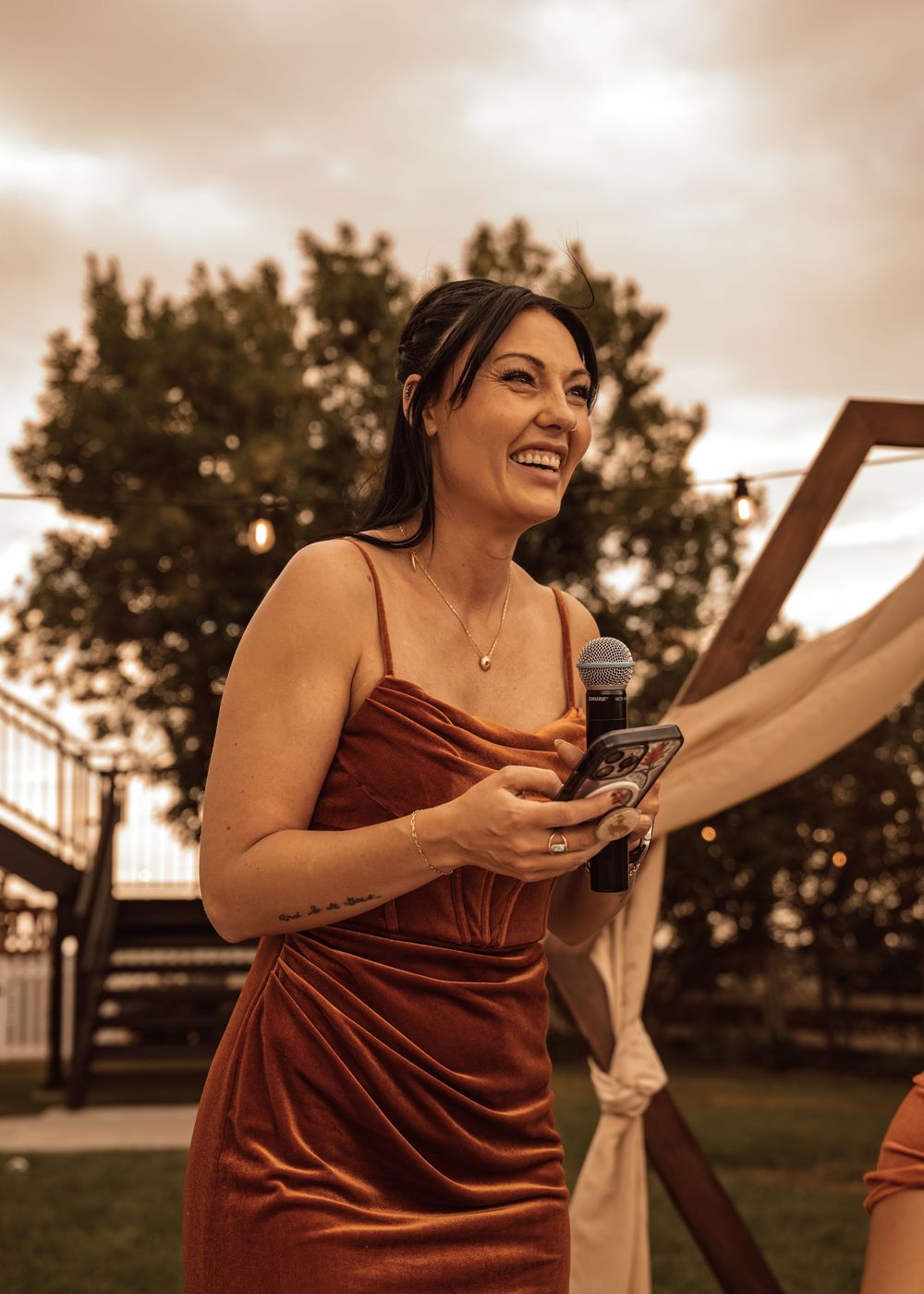 Person in burgundy dress laughing joyfully during outdoor wedding reception.