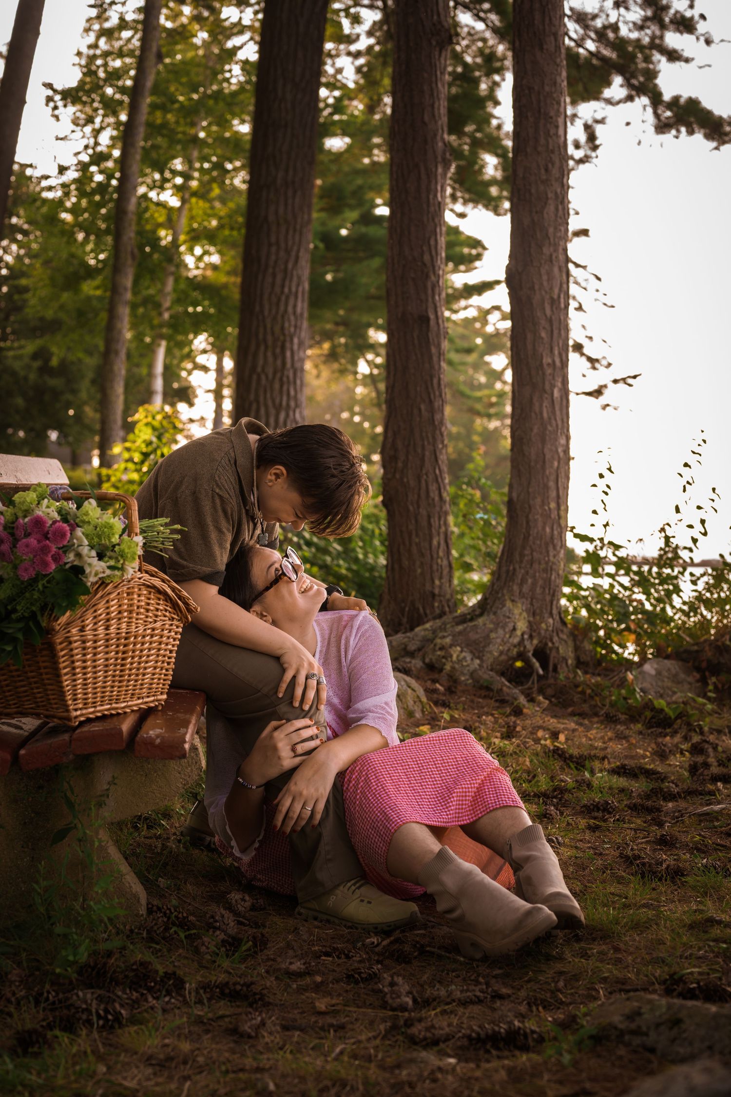 Couple sharing a romantic kiss in a pine forest during a cozy outdoor picnic at sunset.
