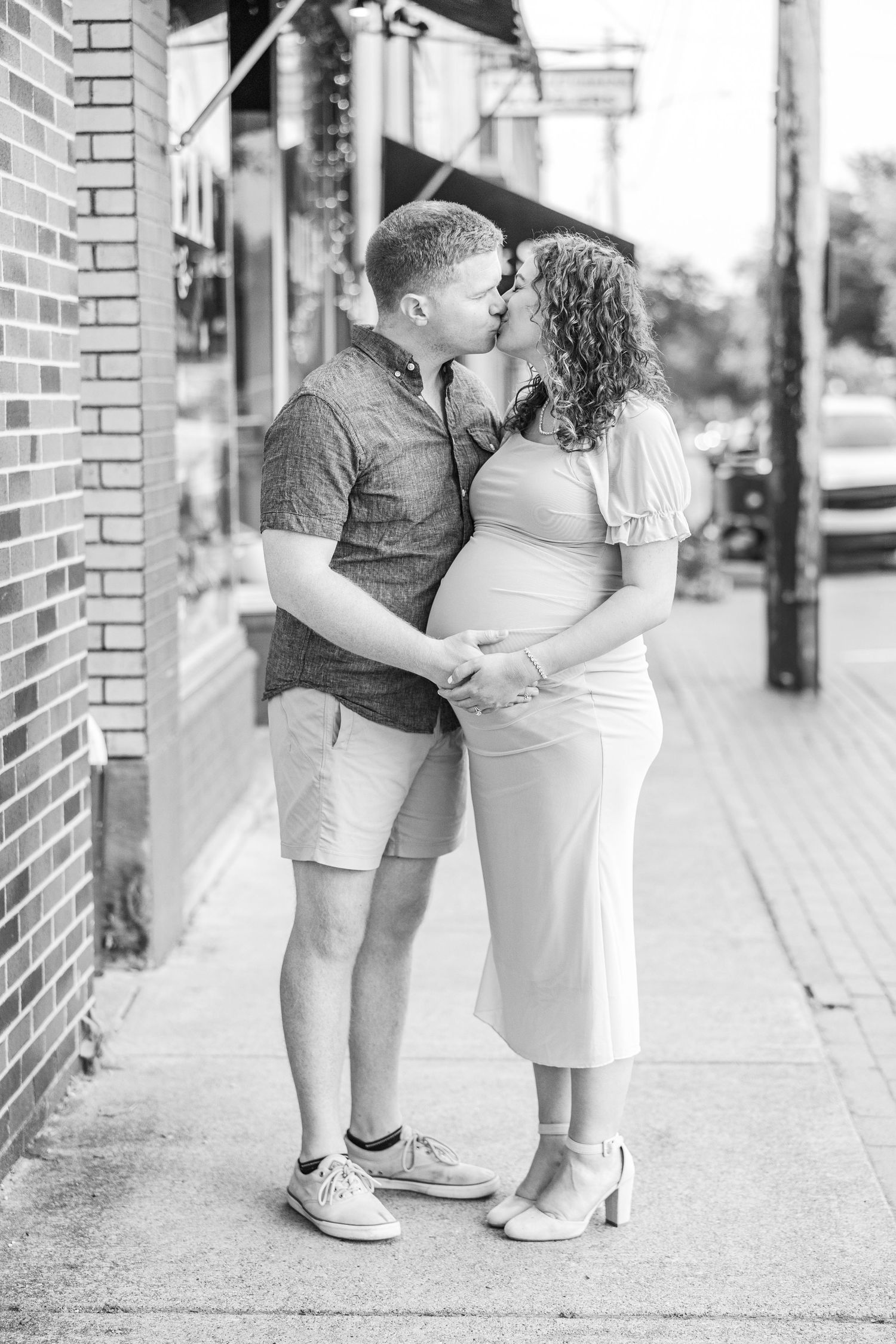 Black and white romantic engagement photos showing a couple embracing on a brick-lined sidewalk.
